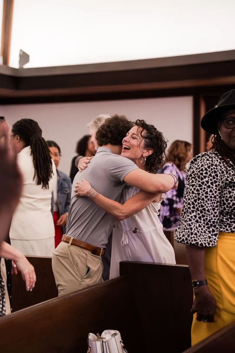 Two people embrace among the sanctuary pews as others greet one another.